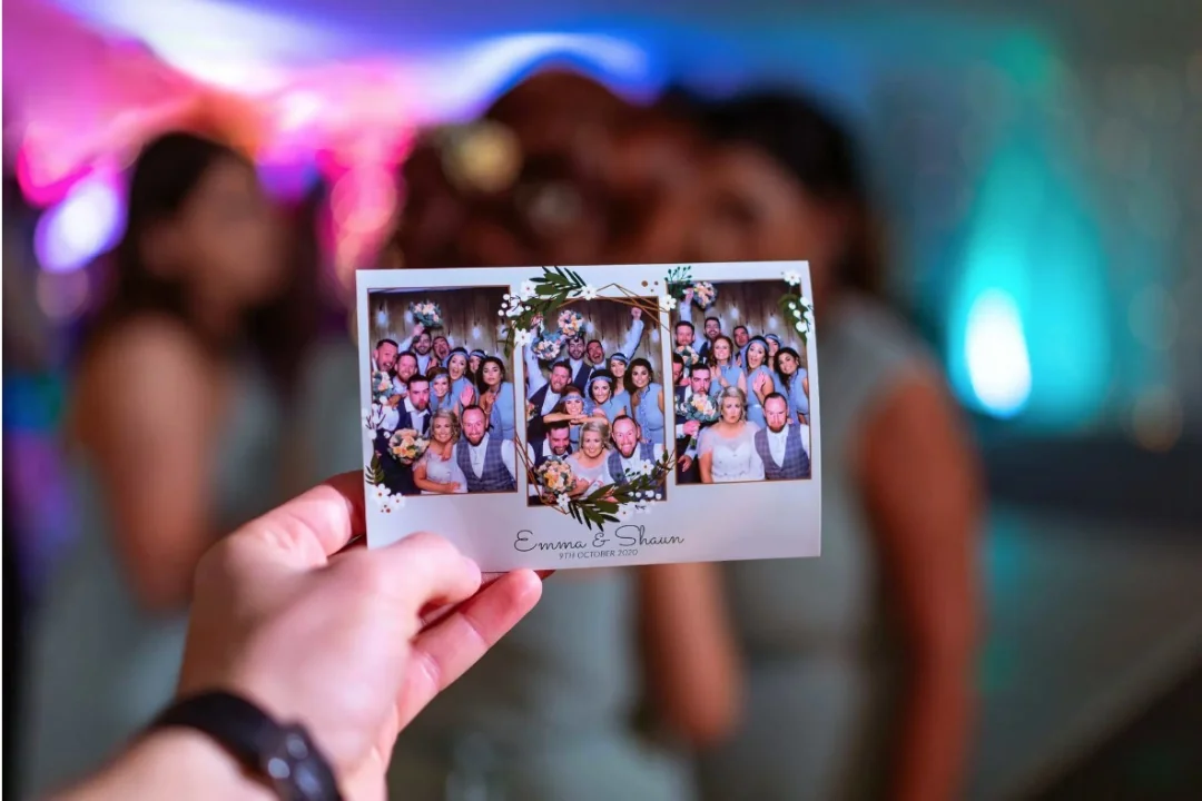 A guest holding a printed group photograph with colorful event lighting behind