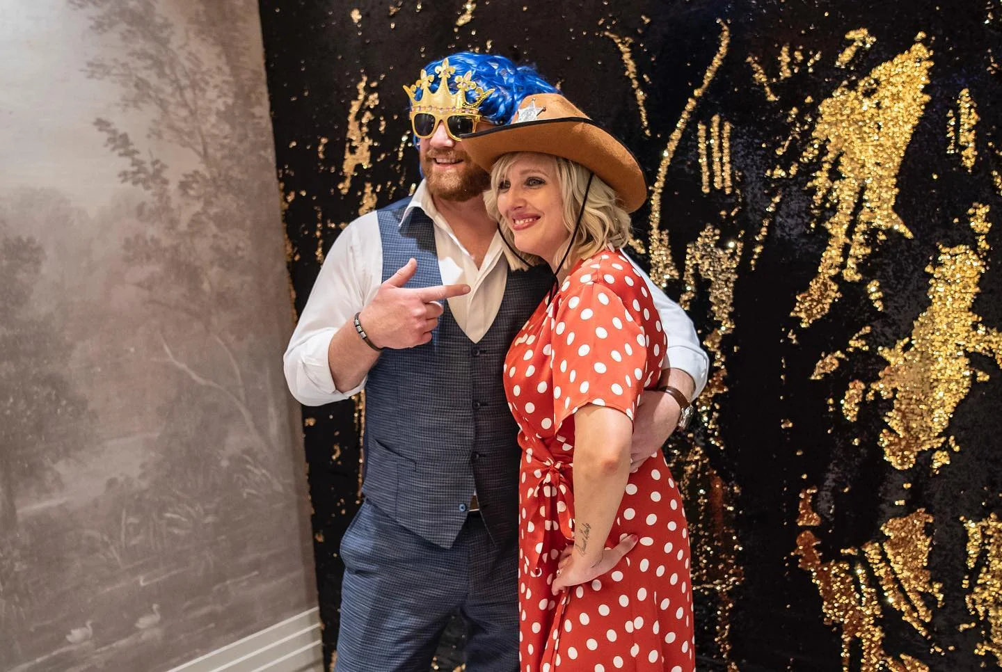 A dressed-up couple laughing with a colorful hat and photo props